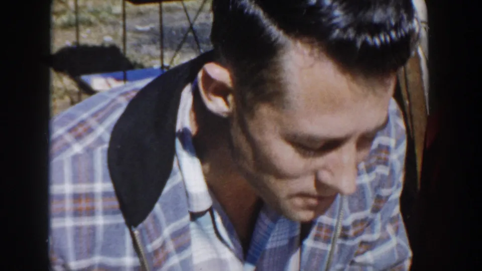 Close-up 8mm frame of a young man in plaid looking down during the Wisconsin outdoor gathering.