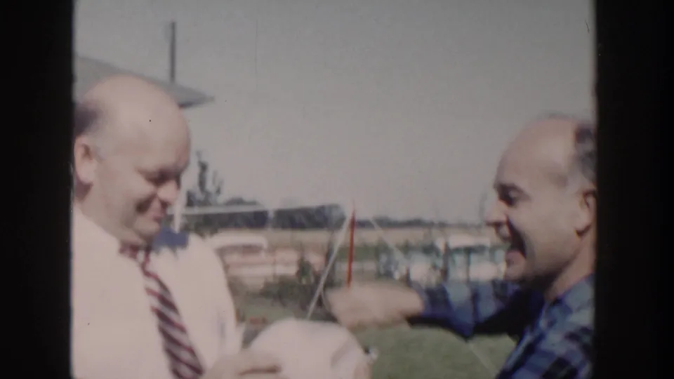 Two adult men appear to laugh and gesture around a white ball in a suburban Wisconsin backyard.