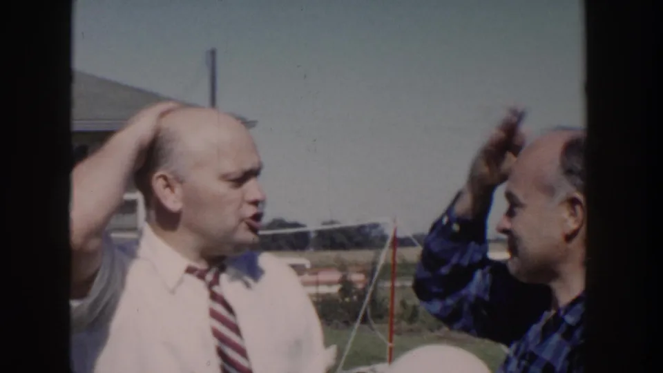 The man in the white shirt and striped tie turns toward the man in plaid during the outdoor 1958 Wisconsin home-movie exchange.