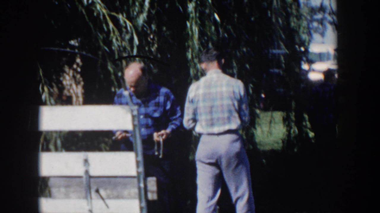 Two men near a white wooden fence or gate in a shaded rural yard.