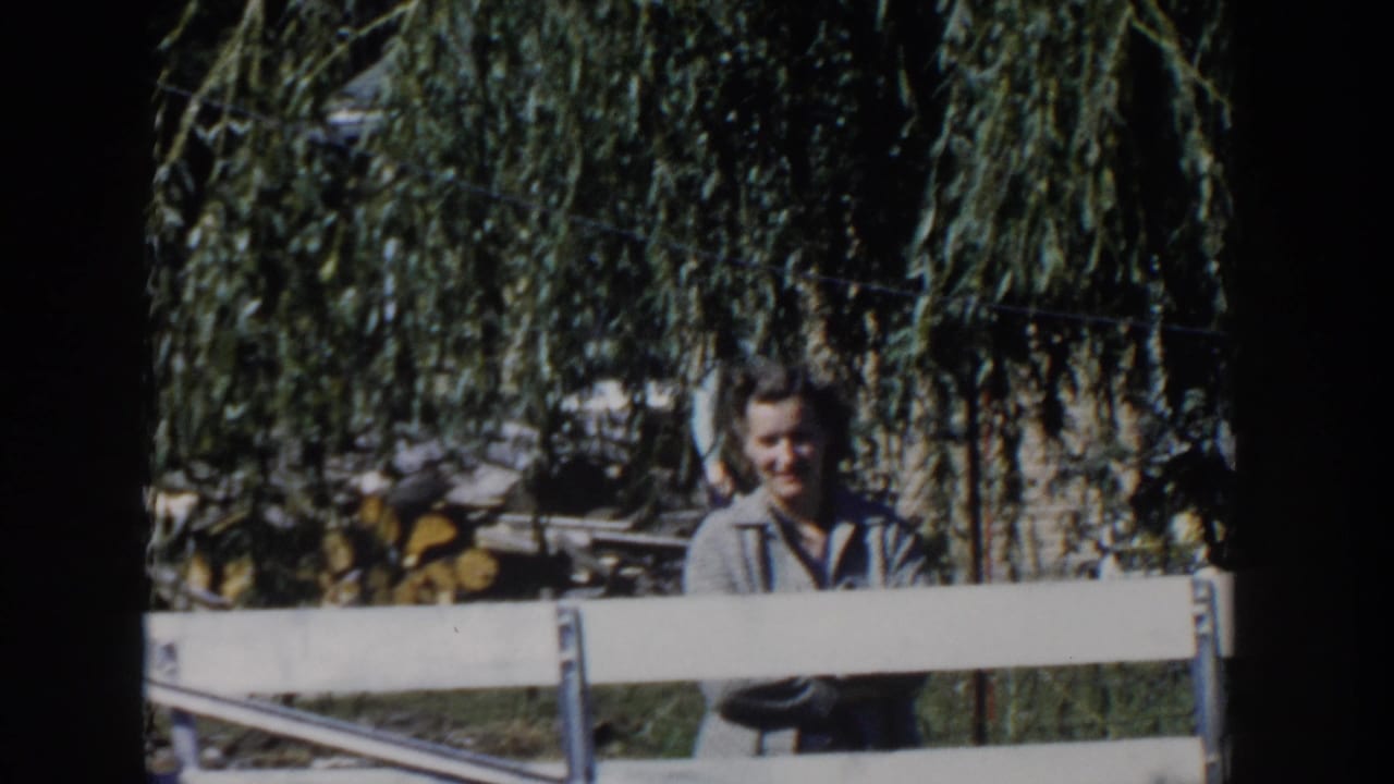 Woman standing behind a white fence under drooping willow branches.