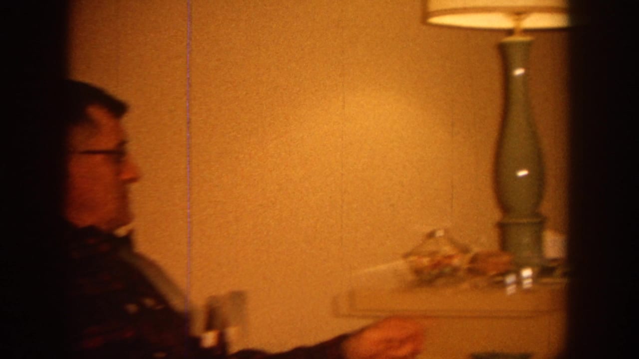 Man in profile seated near a lamp and side table in a living room.