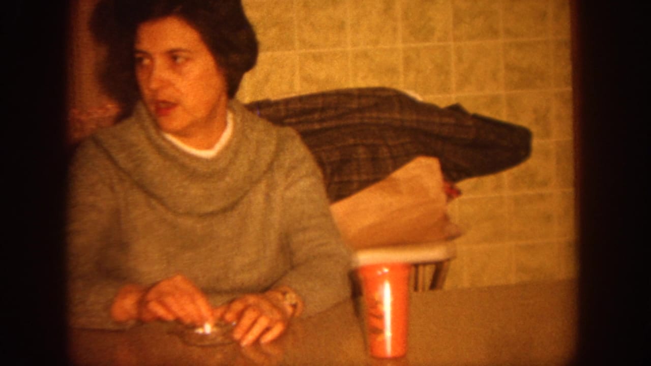 Woman in a gray sweater seated at a table with a red cup and ashtray.