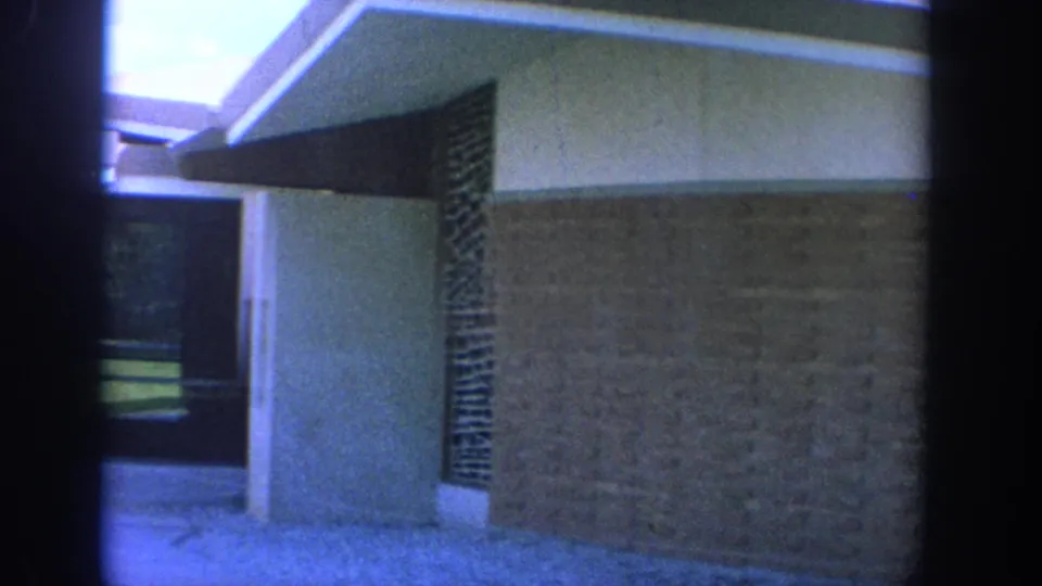 1964 Wisconsin church exterior or corridor view showing brickwork, roof overhang, dark stone screen, and an open walkway.