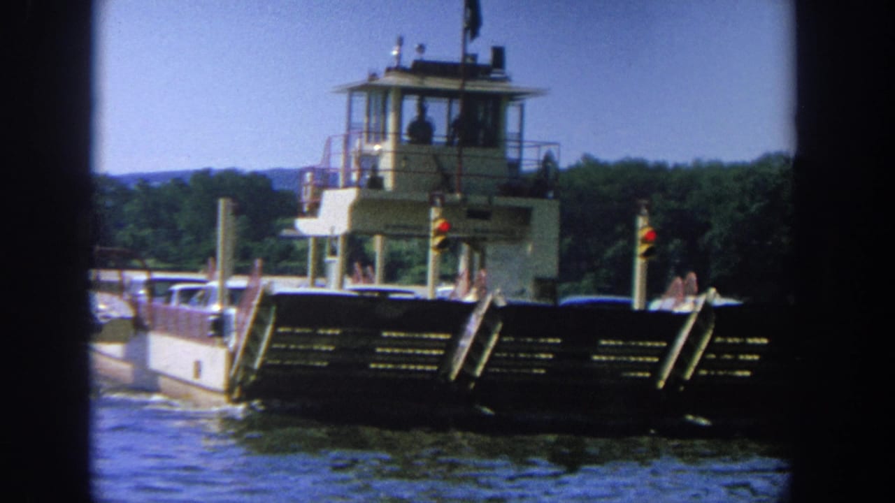 Barge and pilot house seen from the side, with cars on deck and water in front.