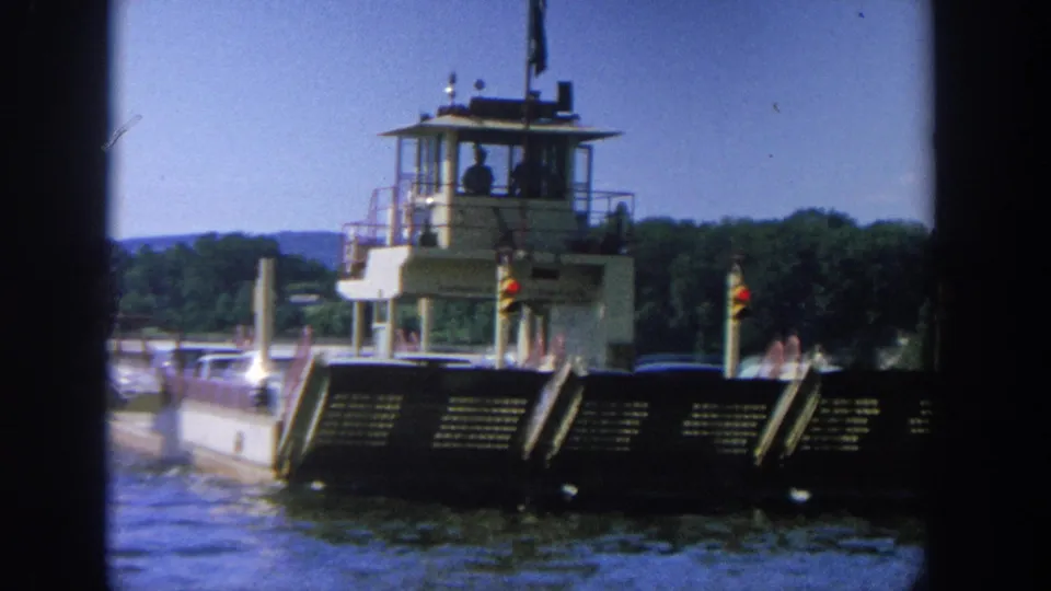 8mm frame of a Wisconsin river barge in 1964, showing cars on the flat deck beneath an elevated pilot house.
