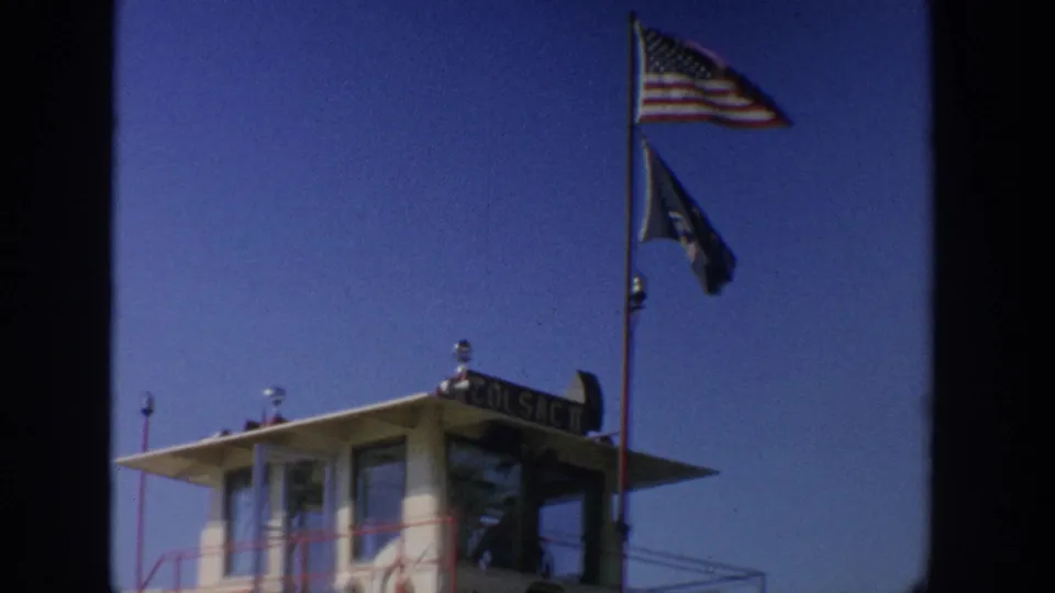 Close 1964 Wisconsin ferry detail showing the pilothouse roof, American flag, secondary flag, and partial vessel name signage.