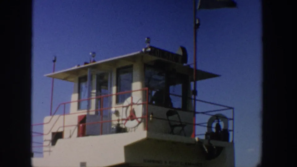 1964 Wisconsin 8mm frame of the ferry pilothouse, red railings, life ring, and partially visible vessel lettering.