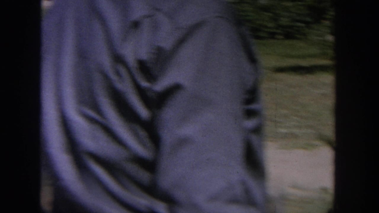 1964 Wisconsin 8mm frame with a blurred close view of a man in a blue shirt beside a backyard lawn and trees.