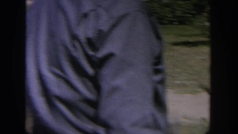 1964 Wisconsin 8mm frame with a blurred close view of a man in a blue shirt beside a backyard lawn and trees.