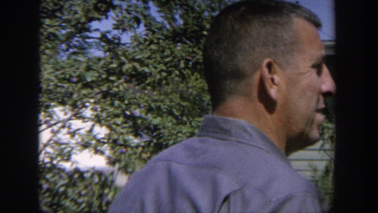 Man in a blue shirt seen in side profile near trees and a house.