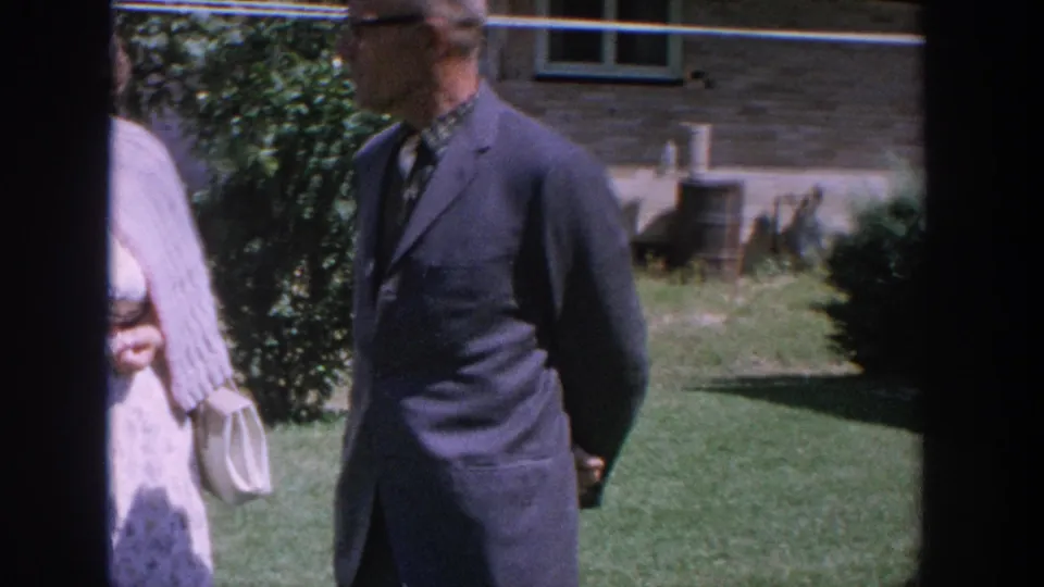 Older couple in a Wisconsin yard, with the man in a dark suit and the woman partly visible near fruit-tree foliage.
