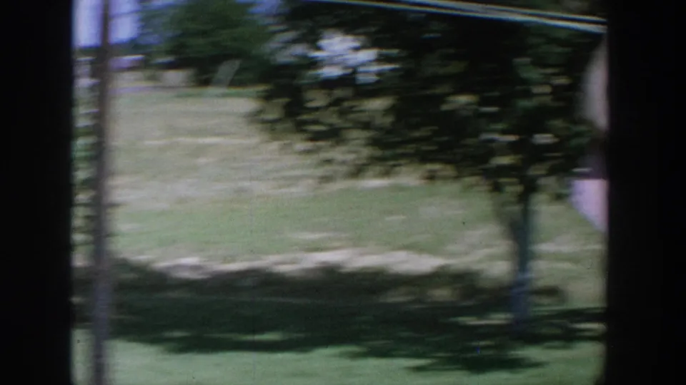 1964 Wisconsin home-movie frame with motion blur across a grassy yard, shrubs, and dark frame edges from the scanned film.
