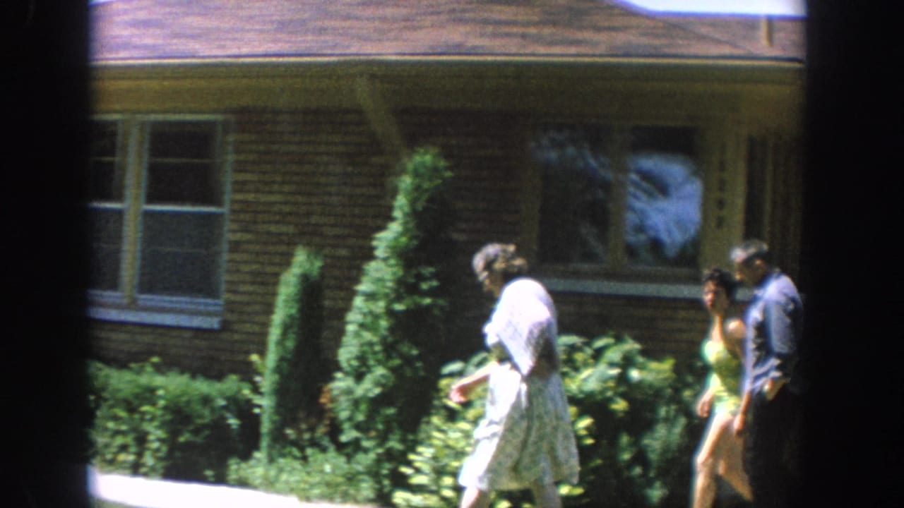 Three adults walking near the front of a brick house.
