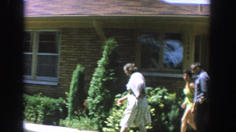 1964 Wisconsin frame with three adults moving along the front lawn and walkway outside a brick suburban house.