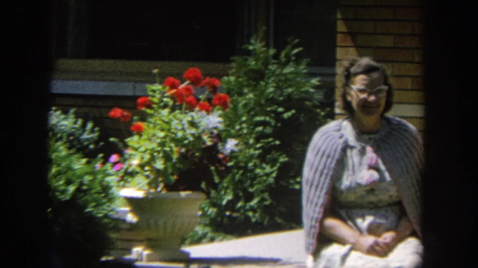 The final frame crops toward one seated woman in glasses near a patio planter, with brickwork, shrubs, and red flowers in view.