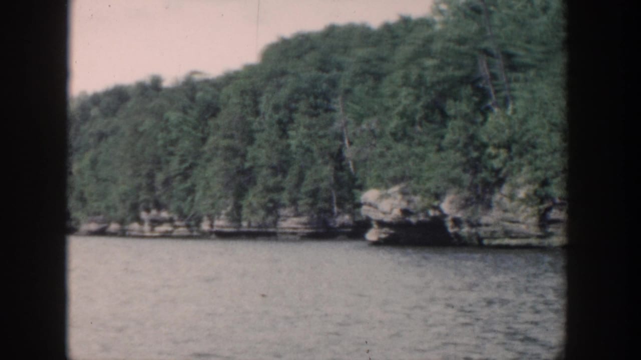Forested rocky shoreline across a lake, seen through dark frame edges.