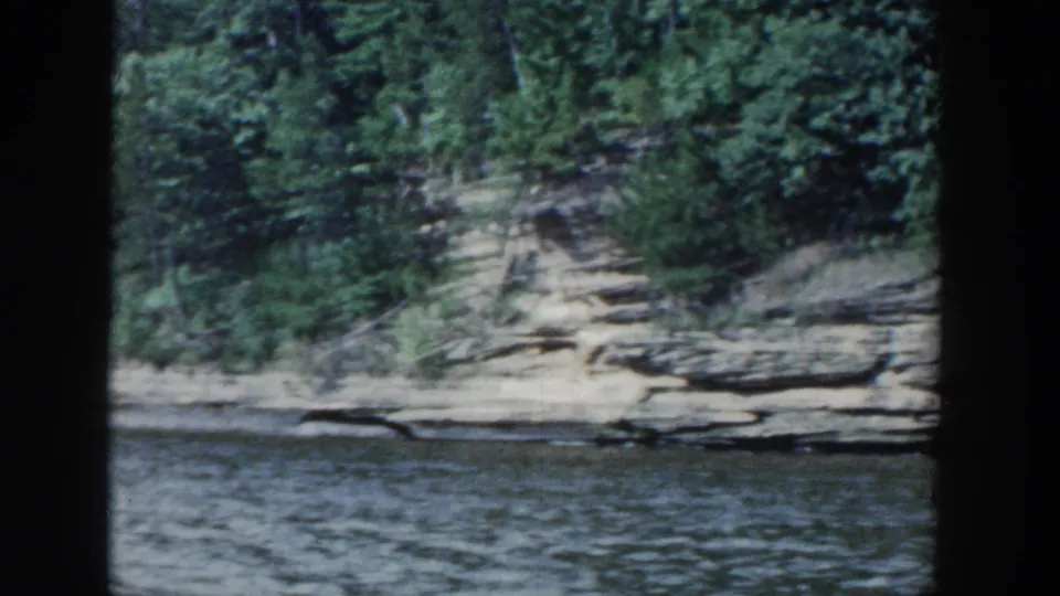 A wooded Wisconsin lakeshore with exposed layered rock appears through the boat interior near the end of the 1964 clip.