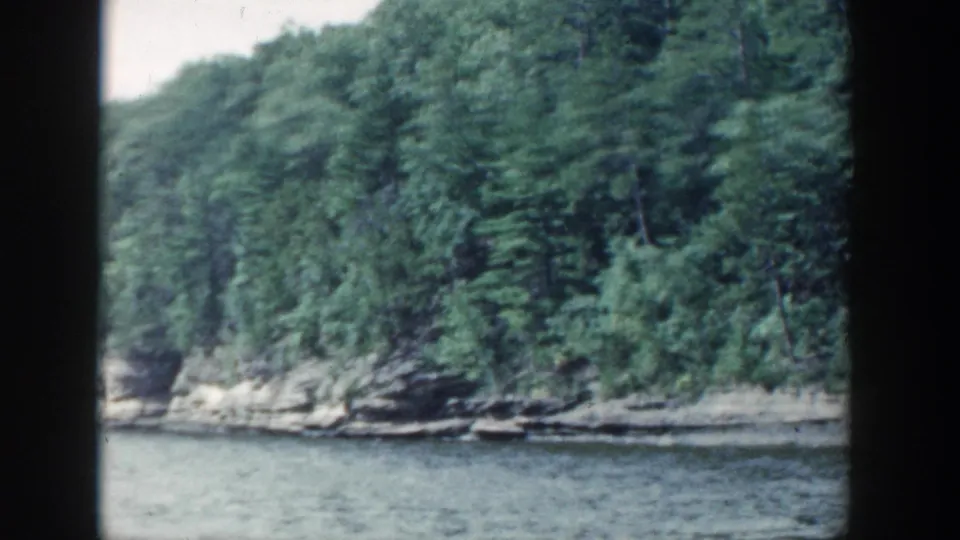 1964 Wisconsin 8mm frame showing a softly blurred wooded slope above calm lake water.