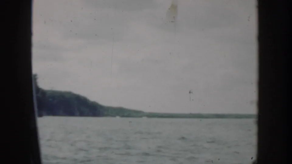 1964 Wisconsin home-movie frame showing open lake water and a low wooded hill beyond, with muted color and visible film wear.