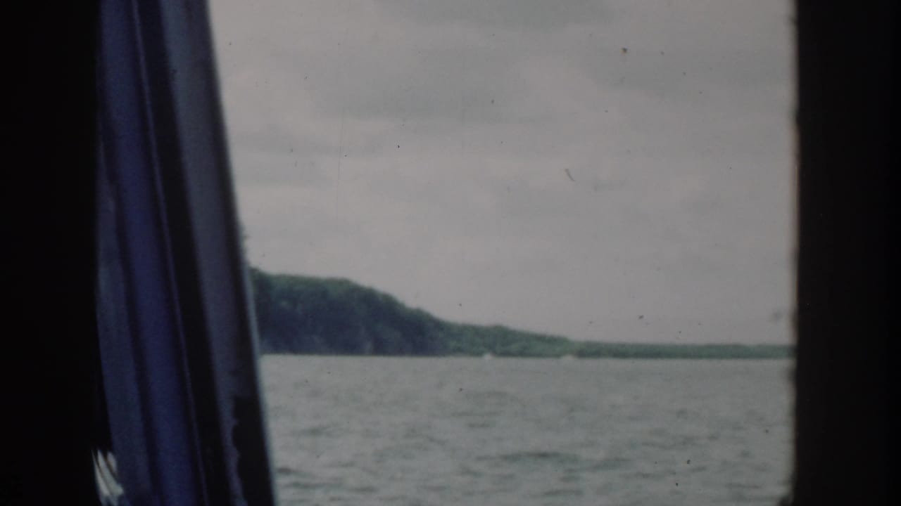 1964 Wisconsin 8mm frame showing calm river water and a distant wooded bank through a dark boat or window opening.