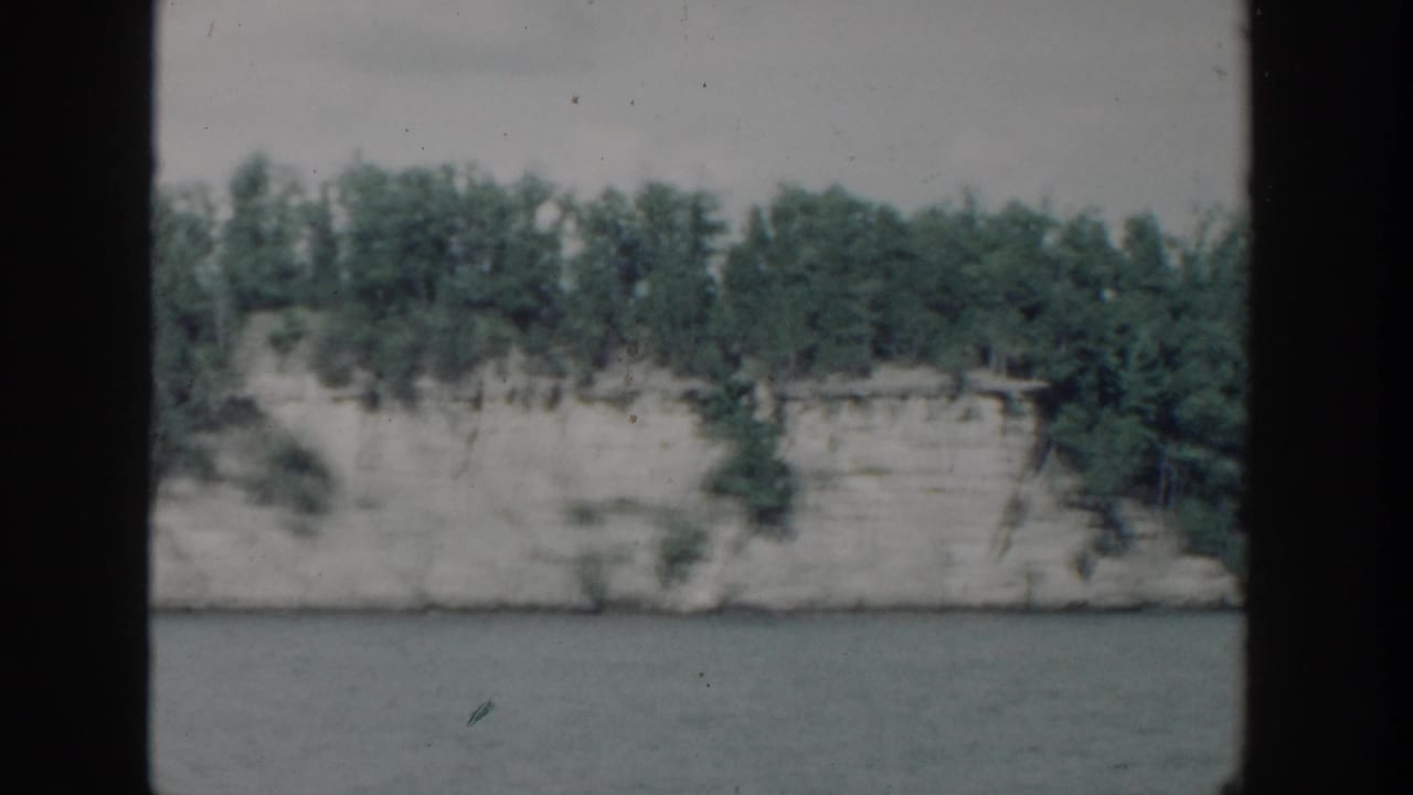 Tree-covered pale bluff beside water with visible 8mm frame edges.