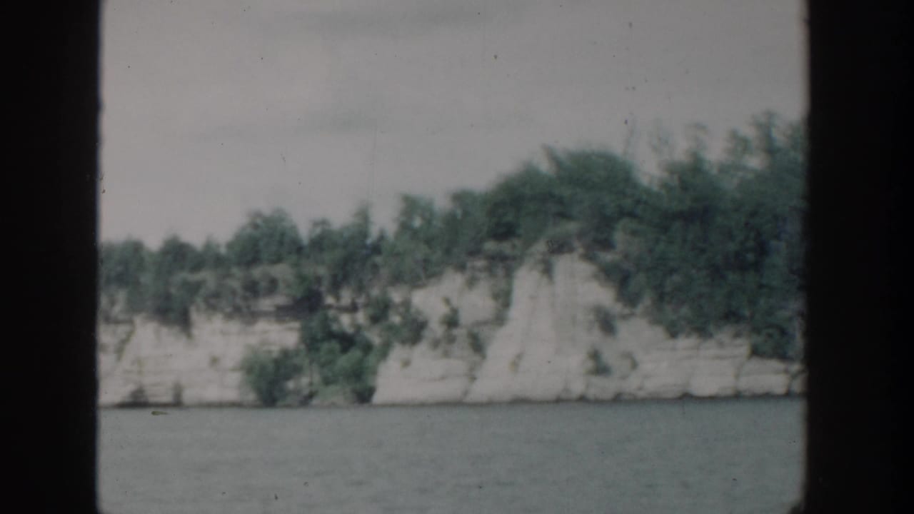 Wooded shoreline cliff across a lake with dark film borders.