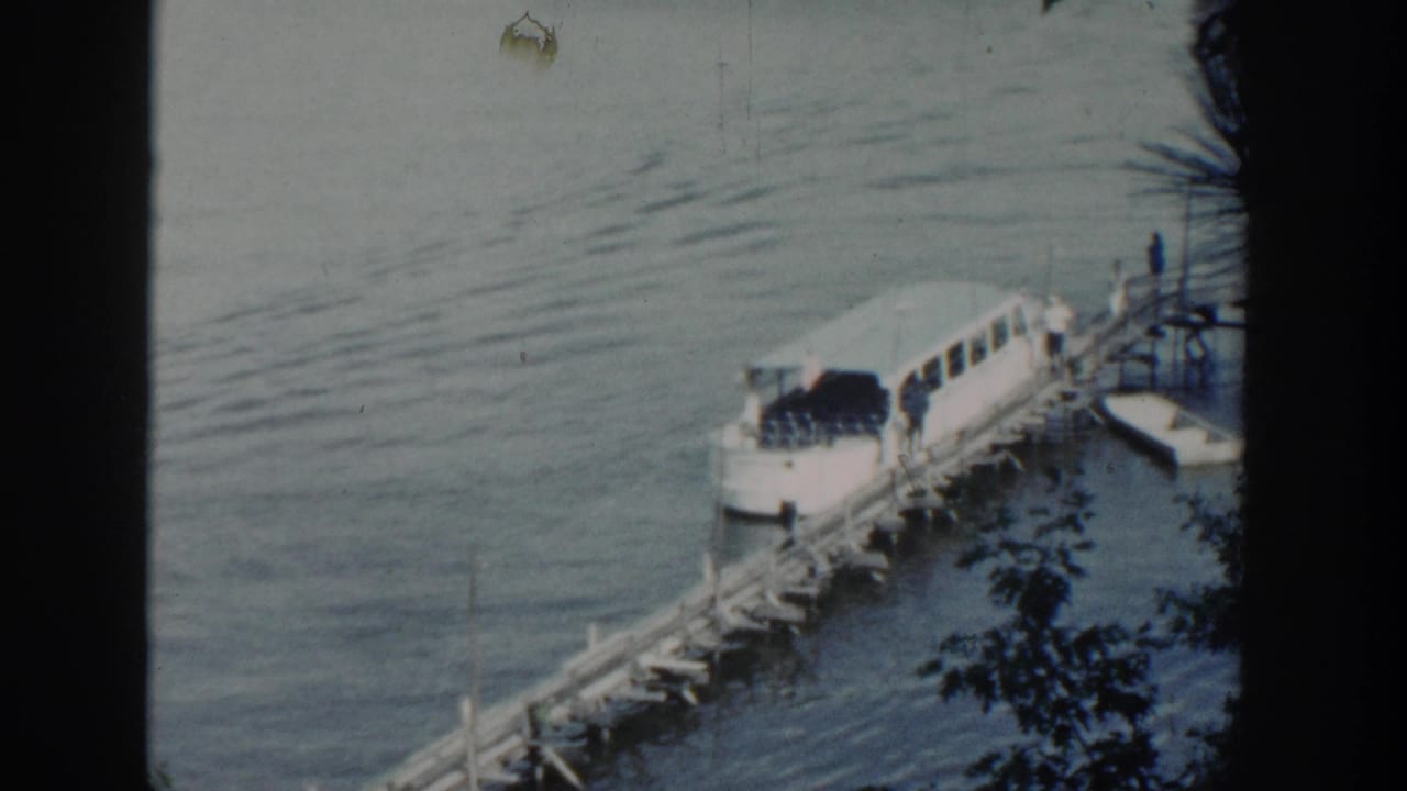 1964 Wisconsin 8mm frame showing a white passenger boat beside a wooden pier on a calm lake, partly obscured by film-frame shadows.