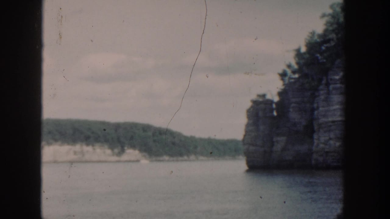 Lake water and wooded cliffs seen through dark boat or window framing.