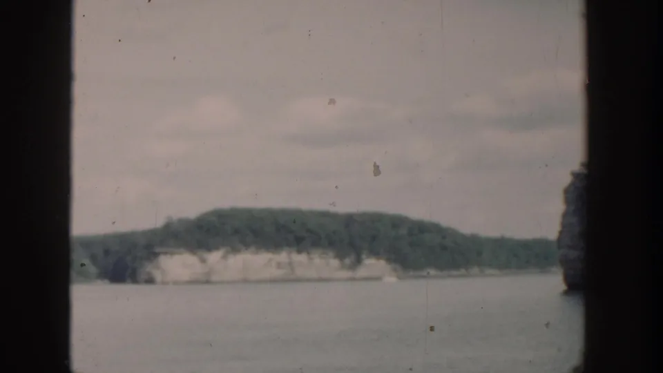 1964 Wisconsin lake landscape with distant pale cliffs, green hills, overcast sky, and dark film-frame edges.