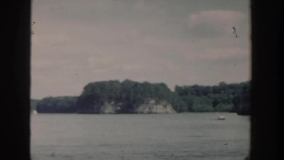 1964 Wisconsin 8mm frame with a broad lake surface and low, tree-covered shoreline in the distance.