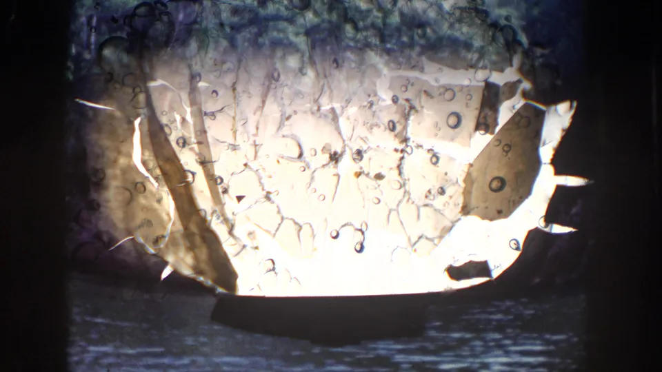 1964 Wisconsin 8mm frame showing film damage over a dark lake view with wooded shoreline and rocky terrain in the background.