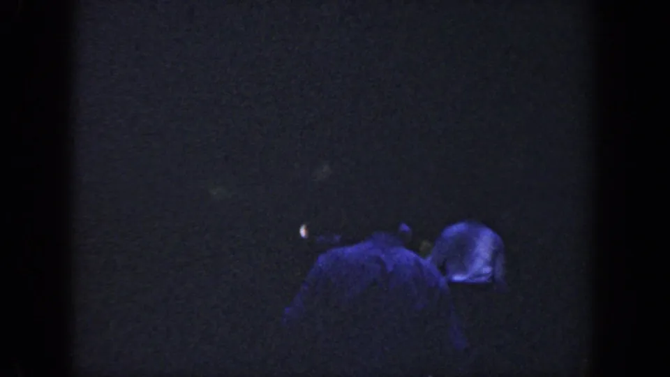Dark 1964 Wisconsin 8mm frame with two shadowed people near the water, their clothing and faces largely indistinct.