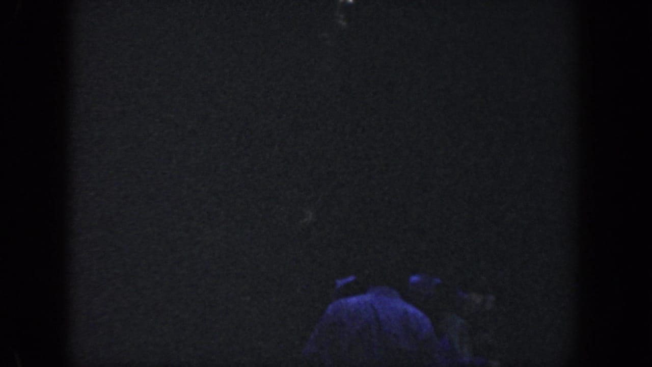 1964 Wisconsin home-movie frame showing a barely visible figure in a light shirt moving through a dark wooded night scene.
