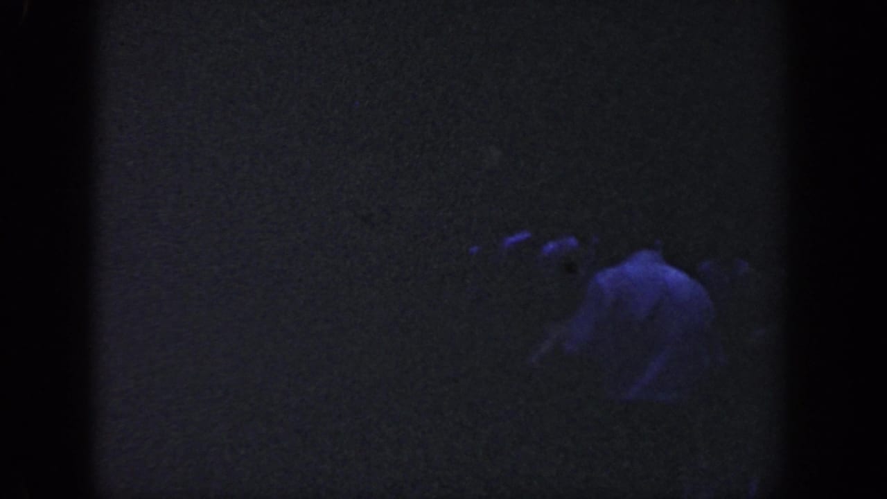 Shadowed figure in a light shirt bending or leaning in darkness.