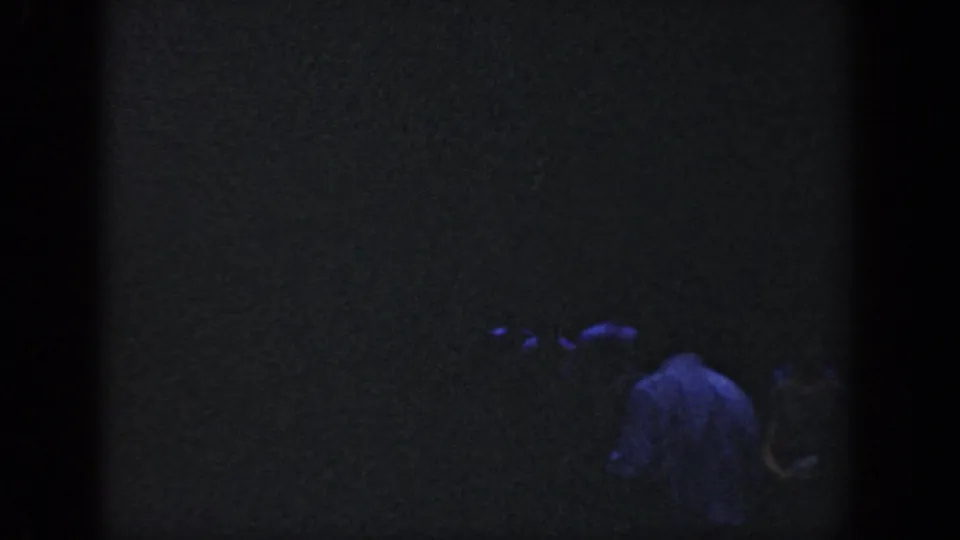 1964 Wisconsin 8mm frame with a person in a pale shirt partly visible at night amid deep shadows.