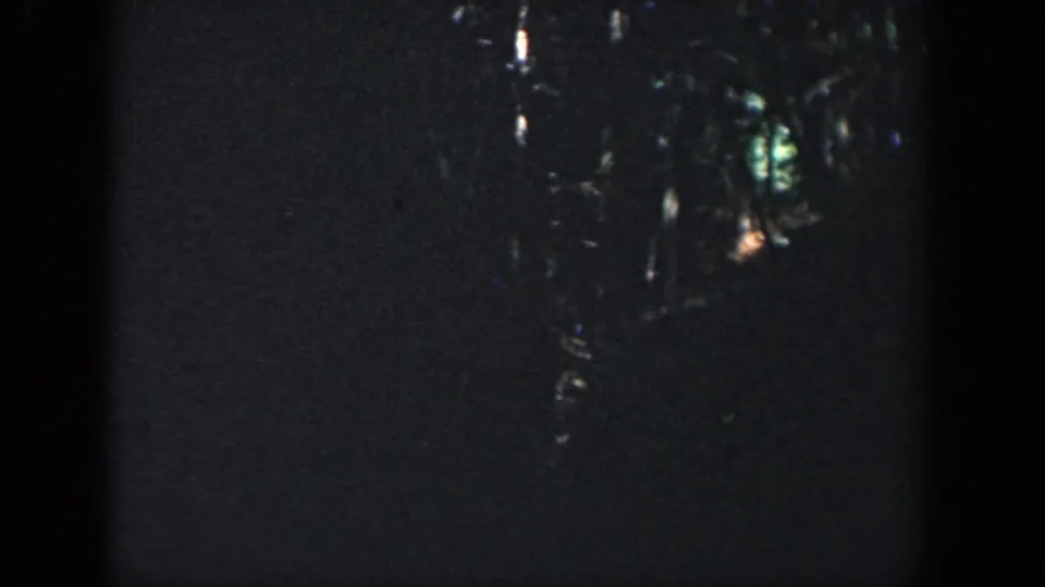 1964 Wisconsin home-movie frame showing reflective points of light and a faint person near the edge of a dark night scene.
