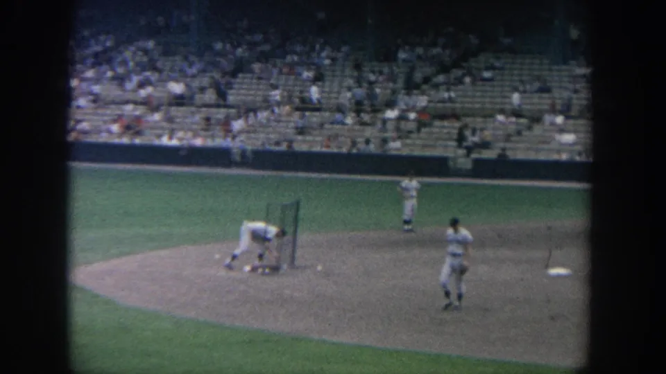 1964 New York baseball scene with a player bending near a protective screen and other players visible across the infield.
