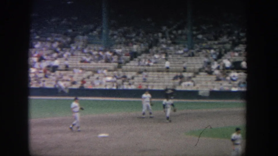 1964 New York 8mm view of players warming up around the infield, framed by stadium seating and film grain.
