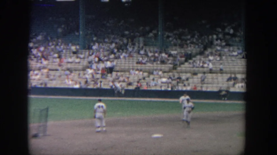 1964 New York home-movie frame showing baseball warmups from the stands, with players and spectators visible.