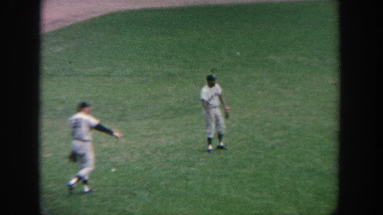 1964 New York 8mm footage shows two baseball players on green outfield grass, with one moving at the left edge of the frame.