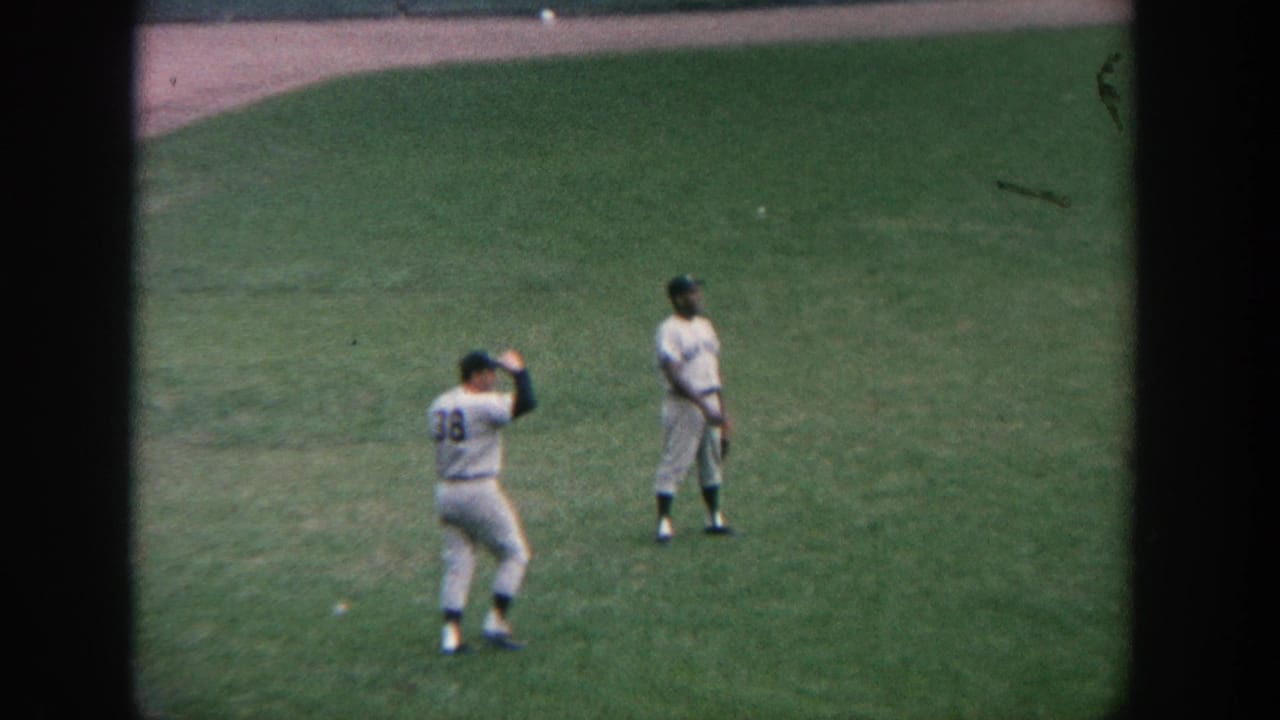 A baseball player wearing number 38 raises a glove near another player on the grass.