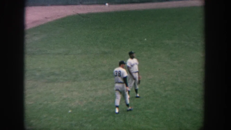 1964 New York 8mm footage shows two baseball players walking close together on the outfield grass, one with number 38 visible.