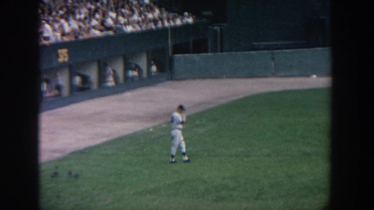 1964 New York stadium view from the stands, with a player crossing the grass near the wall and dugout area.