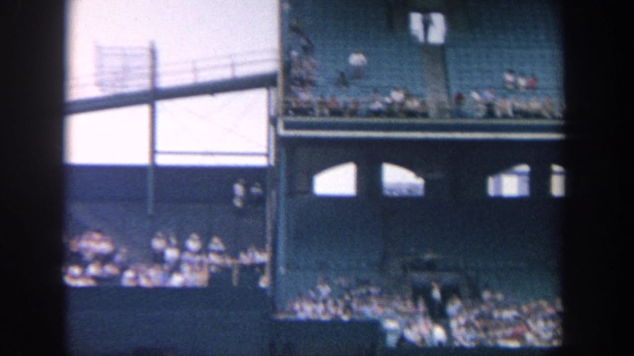 Upper stadium seating, light towers, railings, and spectators seen through a dark film border.