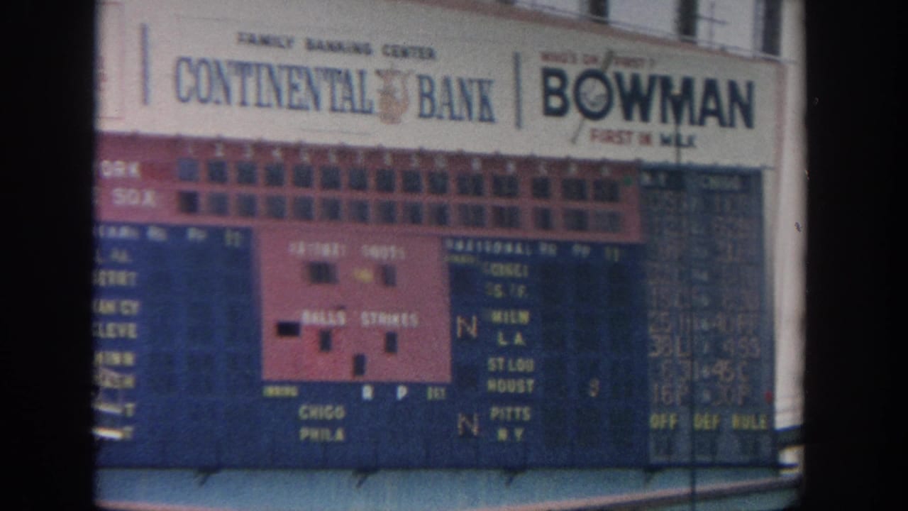 1964 New York stadium view showing a manual baseball scoreboard, blue seating, spectators, and Continental Bank and Bowman Gum signage.