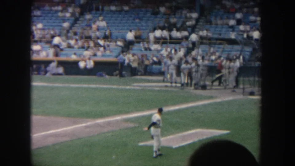 A pitcher stands near the mound in a New York baseball stadium, with dugout players, spectators, and the large scoreboard in the background.