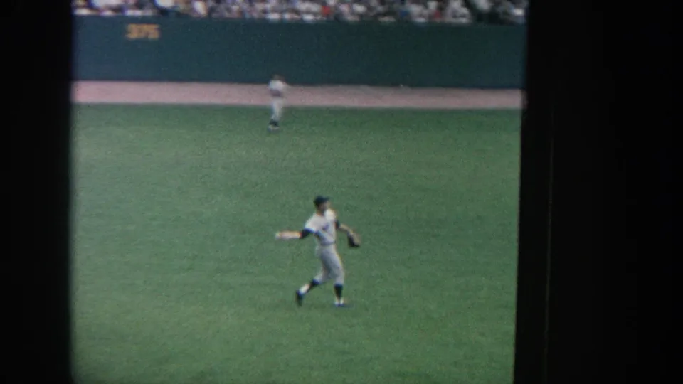 A fielder crosses the green outfield during a 1964 New York baseball game, filmed in soft color from the audience area.