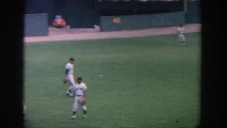 1964 New York baseball game footage shows players in white uniforms and dark caps standing in the outfield area.