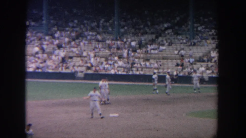 Men in white baseball uniforms pause near the infield in a crowded New York stadium setting from the supplied 1964 footage.